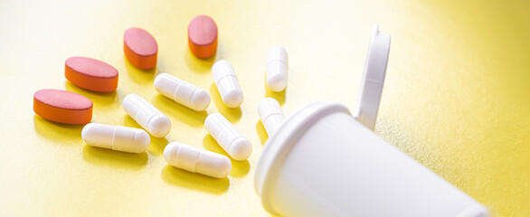 White and red pills are poured from a jar on a yellow background. Food supplement, multivitamins, medications. treatment and prevention of diseases, therapy. wellness. banner