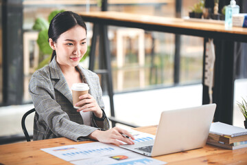 Asian businesswoman working on computer and drinking coffee at the office