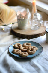 Plate with cookies, open book, lit candles and fairy lights. Hygge at home. Selective focus.