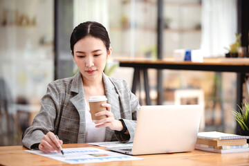 Asian businesswoman working on computer and drinking coffee at the office