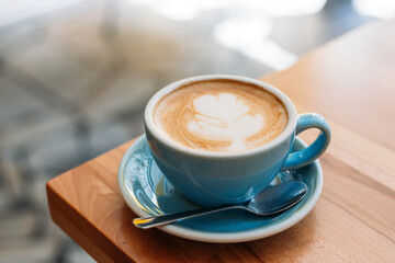 Cup of cappuccino with latte art. Coffee in blue cup on wooden table in cafe. Concept of easy breakfast.