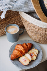 Freshly baked croissant and coffee mug. Coffee in cup on wooden table in cafe. Basket with a gray plaid and a hat, top view