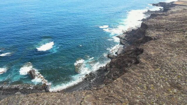 Tilting drone view of a steep volcanic cliff edge with the rough Atlantic Ocean. 3D Structure in a shore cliff on El Hierro, Canary Islands.