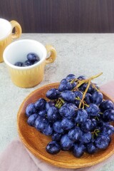In a wooden plate there is a vine with ripe dark-colored fruits and a stone inside