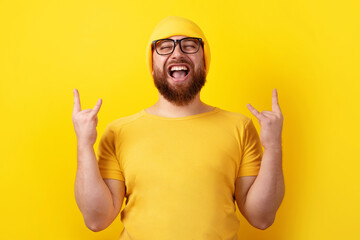 positive man makes rock n roll gesture over yellow background, people and body language concept