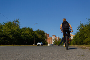 A child on a bicycle rides after athletes on roller skis riding along a wide road to the city from the park