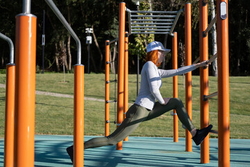 athletic ginger woman warming up for morning training outdoor on urban sports ground in autumn sunny day