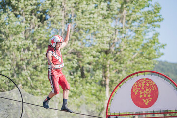 street circus. Circus person with red suit and helmet balancing on the wire