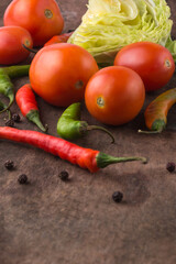 organic vegetables on a wooden surface, tomatoes, green and red chilies, cabbage with black peppers, closeup view with copy space taken in shallow depth of field 