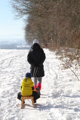Fototapeta na wymiar Frau zieht einen Schlitten mit Kind durch die verschneite Winterlandschaft