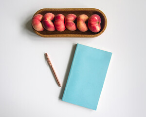 Creative office style table, blue notepad cover, rose-gold pen and ripe flat donut peaches in cork...