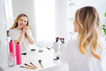 Obraz na płótnie Canvas Portrait of attractive cheerful blond girl looking at mirror enjoying morning rest makeup procedure at light white home indoors