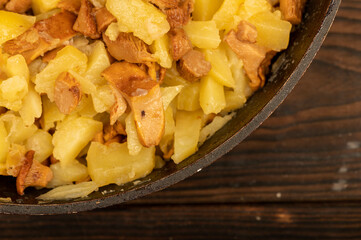 Potatoes fried in a frying pan with mushrooms on a wooden table. A traditional village dish.