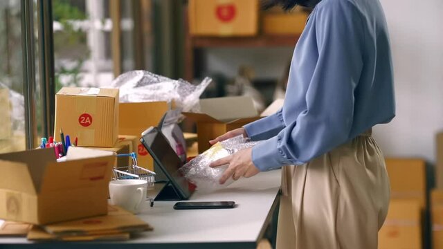 Closeup hand of worker or seller cover ceramic coffee cup with air bubble wrap for protection product broken. Shipping order box for dispatching. Business online and shipping service.