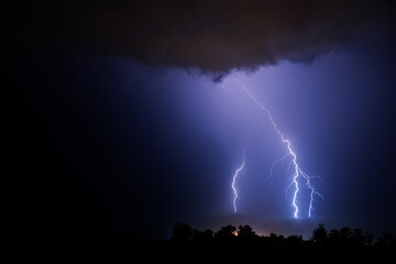 Fototapeta na wymiar Three powerful lightning bolts during a night thunderstorm over the sea.
