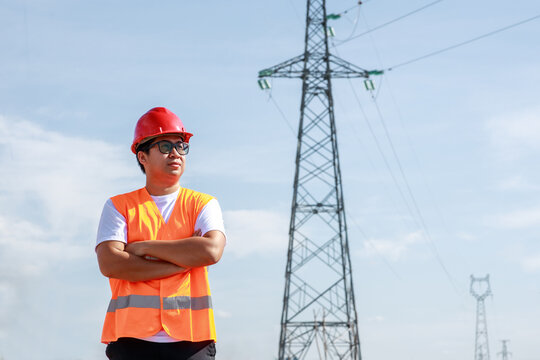 Asian electrical engineers worker in standard safety uniform standing at a power station to working inspect the electricity high voltage pole.