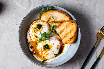 Cilbir or Turkish Eggs. dish served as mezze: poached eggs topped over herbed greek yogurt, then drizzled with hot spiced paprika olive oil. Turkish breakfast in a grey bowl on marble background