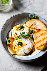 Cilbir or Turkish Eggs. dish served as mezze: poached eggs topped over herbed greek yogurt, then drizzled with hot spiced paprika olive oil. Turkish breakfast in a grey bowl on marble background