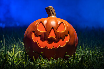 Obraz premium Spooky Scary Orange Pumpkin Creepy Laughing Tooth Smile in Green Grass with Misty Foggy Blue Background