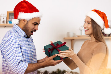 Romantic multiethnic couple in Christmas hats exchanging gifts