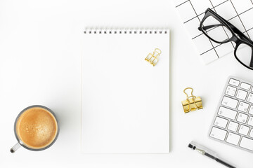 Blank notepad, cup of coffee, keyboard, eyeglasses, pen, notebook, binder paper clip on white background. Modern blogger workspace mockup. Online business or education concept. Copy space, flat lay.