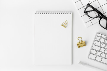 Keyboard, glasses, blank notepad, binder paper clip, pen, notebook on white background. Business concept mockup. Freelancer online office with stationery supplies. Copy space, top view, flat lay.