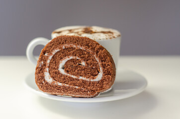 Chocolate sponge roll with a vanilla flavour filling and fresh coffee in the cup, chocolate swiss roll