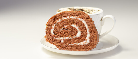 Chocolate sponge roll with a vanilla flavour filling and fresh coffee in the cup, chocolate swiss roll