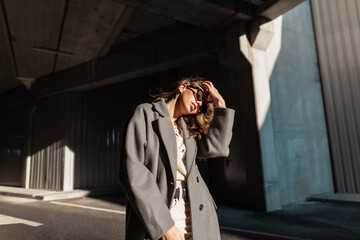 fashionable portrait of a beautiful girl with sunglasses in a vintage coat with a sweater straightens her curly hair in the city. Urban casual feminine style and beauty
