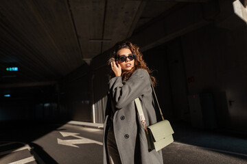 Fashionable beautiful young woman with curly hair and stylish sunglasses in a fashionable long coat...