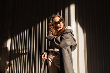 Fashion portrait of a beautiful young curly-haired woman with sunglasses in a stylish coat on the...