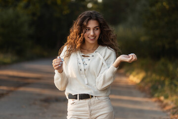 happy portrait of lovely young curly woman with a smile in a knitted fashionable sweater walks in the park outdoors. Female cute face