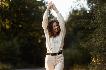 Young curly happy pretty woman with a smile in fashionable knitted clothes walks in nature. Female smiling face