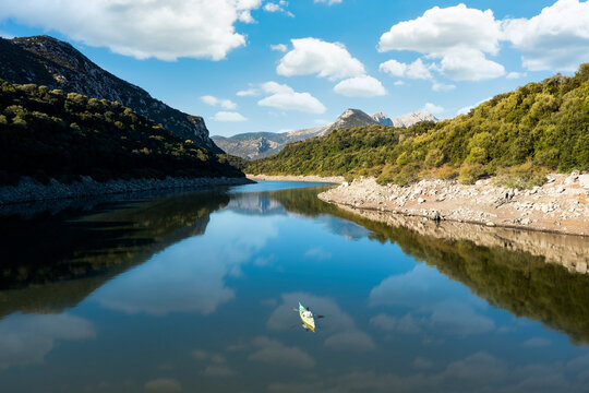 View from above, aerial view of a person paddling a canoe - kayak on the Cedrino Lake surrounded by the mountain range of Supramonte located northeast of the Gennargentu massif. Sardinia, Italy.