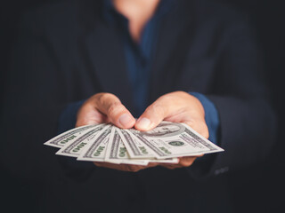 Hand of a businessman holding US dollars banknote with a black background while standing in the studio. Close-up photo. Space for text