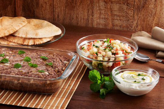 Quibe assado com guarnição de salada e coalhada, em mesa de madeira
