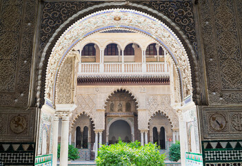 Beautiful arabian style decorated arch in the famous Alcazar (meaning: fortress) in Seville, Andalusia, Spain. A patio with green plants in the middle.