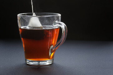 Black tea in a triangular pyramid tea bag is brewed in hot water in a transparent mug. Dark...