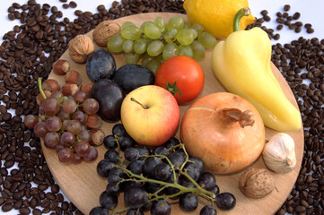 Fresh vegetables and fruits on the kitchen board. There are onions, lemon, grapes, plums, nuts, hazelnuts, tomatoes, paprikas, apples. Around these are coffee beans.
