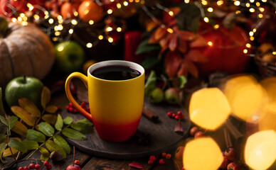 Obraz na płótnie Canvas red and yellow mug with mulled wine. Fruits and spices are all around on a wooden table. Yellow lights of garlands are burning behind
