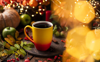 red and yellow mug with mulled wine. Fruits and spices are all around on a wooden table. Yellow lights of garlands are burning behind