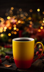 red and yellow mug with mulled wine. Fruits and spices are all around on a wooden table. Yellow lights of garlands are burning behind