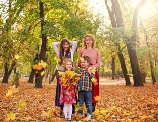 Family with three children actively having fun in autumn park with fallen yellow foliage, seasonal holiday weekend