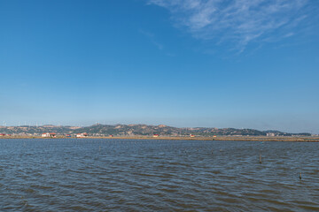 The coastline under the blue sky, opposite the sea are mountains and wind power