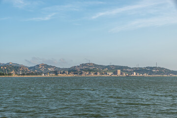 The coastline under the blue sky, opposite the sea are mountains and wind power