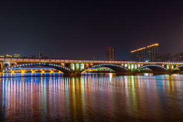 In the city at night, colorful lights are reflected in the water of the river