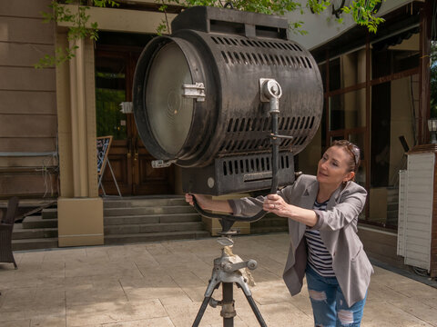 The girl is holding on to a large movie projector with her hands.