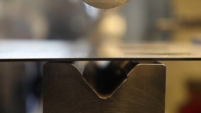 The process of bending a metal part on a bending machine. Bending metal with a large radius using a radius punch and a die, close-up 