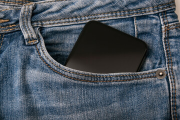 A black smartphone in the pocket of blue jeans, people comunication concept
