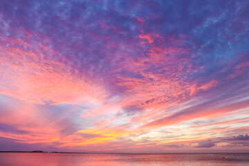 Fototapeta na wymiar Glorious beautiful colorful sunset with colors stringing out from horizon over ocean with yellow and pink bursting into dappled purple near the top